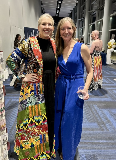 Woman in colorful coat standing next to a woman in a blue jumpsuit
